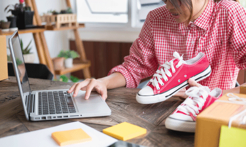 A woman using a laptop to list a pair of trainers on Ebay to sell.