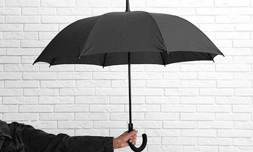 Person holding a black umbrella in front of white brick wall