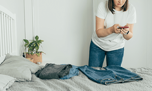 woman taking photo of jeans on bed